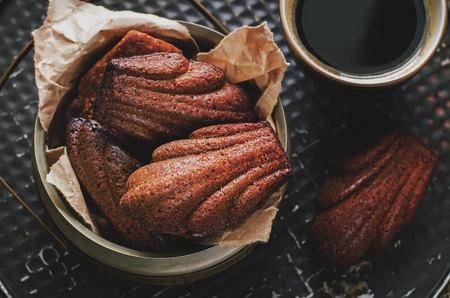 chocolate cookies in the shape of shells, Madeleine, and a cup of coffee on a dark background. tinting. selective focus on biscuitsの写真素材