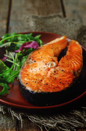 grilled salmon on a salad of arugula on a dark wood background. tinting. selective focusの写真素材