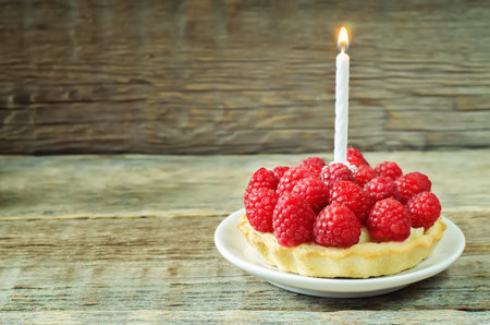 tartlet with raspberry and cream cheese and a candle on a dark wood background. tinting. selective focusの写真素材