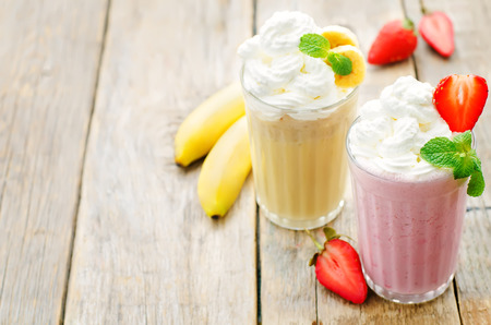 strawberry and banana milkshake with whipped cream on a dark wood background. tinting. selective focusの写真素材