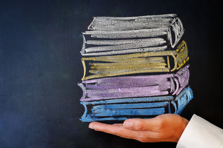 Man\'s hand holding a stack of books drawn with chalk on a black backgroundの写真素材