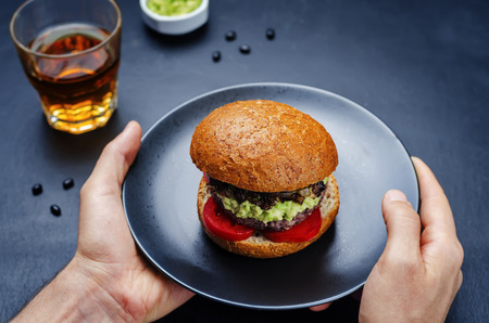 Men's hands holding the black bean burger with mashed avocado, caramelized onions and tomatoes. toning. selective focusの写真素材