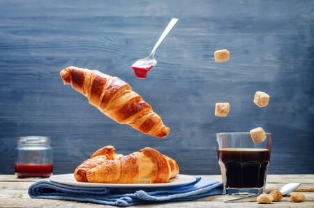 Flying croissant with coffee and jam on a wood background. toning. selective focusの写真素材