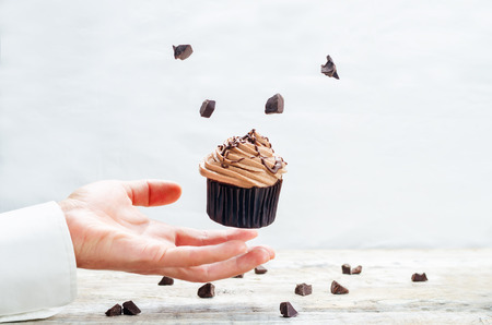 Male hand with flying chocolate cupcake. toning. selective focusの写真素材