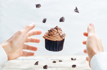 Male hand with flying chocolate cupcake. toning. selective focusの写真素材