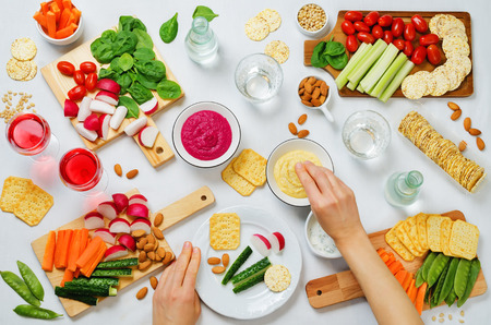 Women's hands and variation of healthy vegan snacks. Vegetables, crackers, dip and hummus. toning. selective focusの写真素材