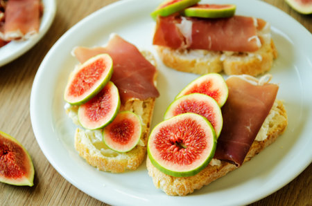 Figs goat cheese prosciutto crostini on a wood background. toning. selective focus