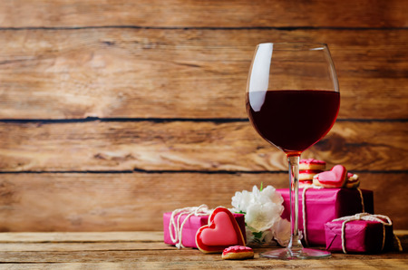 Glass of red wine with heart shape cookies, flowers and gifts on a wood background. toning. selective focusの写真素材