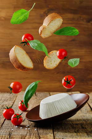 ricotta cheese with flying bread slices, tomatoes and Basil on a wood background. the toning. selective focusの写真素材