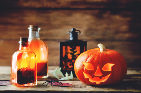 Glowing pumpkin with jars on dark wood background. Halloween concept. Toning. Selective focusの写真素材