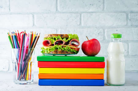 school lunch background with a sandwich, fresh fruits and multicolored books. toning. selective focusの写真素材