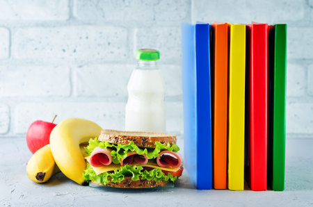 school lunch background with a sandwich, fresh fruits and multicolored books. toning. selective...