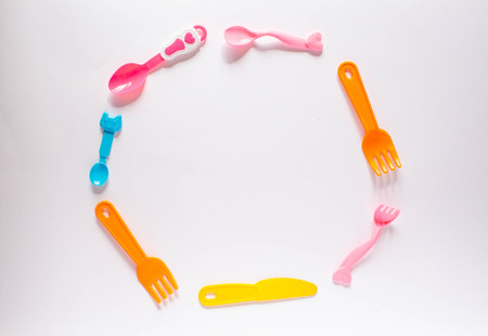 Children plastic dishes on a white background, forks, spoons, plate, food with space for text. Flat lay, top viewの写真素材