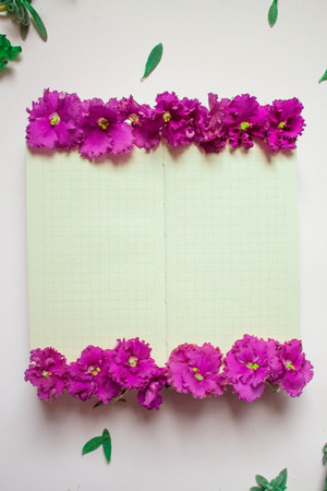 Empty notebook decorated purple flowers on a white background, top view. Notepad decorated with green leaves and violet. Flat layの写真素材