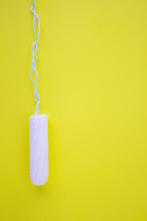 One swab with cotton on a yellow background. The concept of the period of the menstrual cycle. Top view, flat layの写真素材