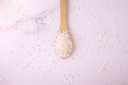 rice in a wooden spoon on a white marble. space for text, layout. Fashionable, modern photo.の写真素材