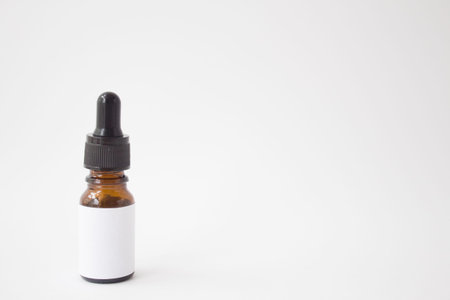 Dropper glass Bottle Mock-Up. Oily drop falls from cosmetic pipette on white backgroundの写真素材