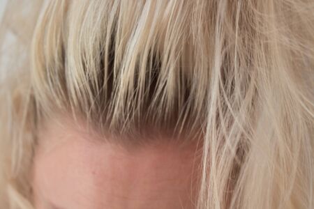 Closeup of a woman's blond head with parted hair regrown roots. Haircare, making new hairdo, hair therapy concept.の写真素材