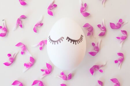 Easter eggs on a white background in pink spring flowers with copyspace. Minimalism concept, Top view. Mock up. Flat lay.の写真素材