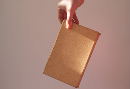  book in the hand of a girl with a beautiful shadow on a white and gray background. beige book in...