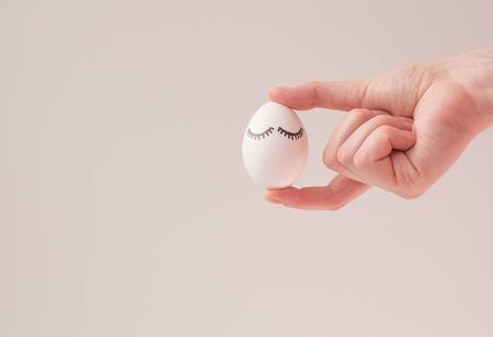 Easter layout on a white background. An egg with painted eyes in the hand of a young woman. Card with copy space.の写真素材