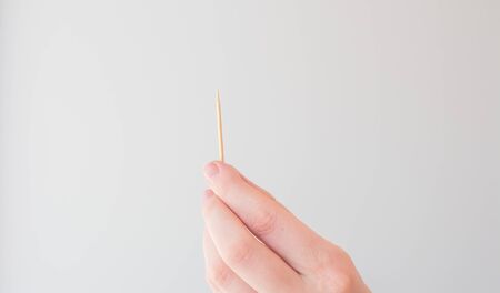Toothpick in female hand on white background. The concept of dental hygiene, oral health. Card with copy space for text.の写真素材