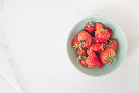 Strawberries in a green ceramic plate on a white marble table. Card with copy space for text. Top view, flatlay.の写真素材