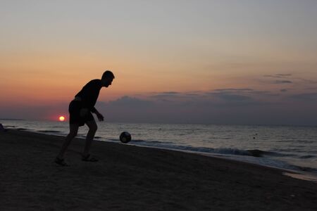 Silhouette of guy on the seashore at sunset plays the ball. Unity with nature and filling with vitality. Summer concept.の写真素材