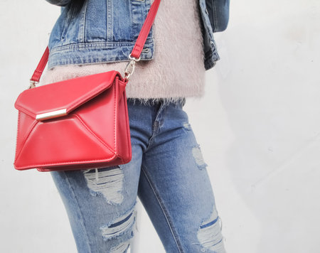 Girl with a small fashionable red bag over her shoulder in a denim suit. Close-up modern red handbag. の写真素材