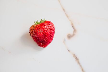 One ripe red strawberry on a white marble table. Stylish photoworks, minimal and summer concept, summer berries.の写真素材