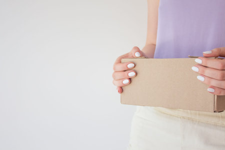 Beautiful girl with a parcel in hands, delivery concept. White manicure, box with order