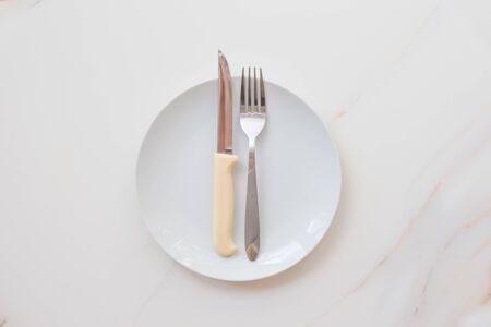  Empty white plate with cutlery on a marble table, saucer, fork and knife. The concept of diet, fasting.の写真素材