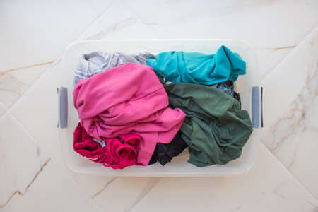Rectangular basket with dirty linen on a white marble floor close-up, top view. Bright underwear of different colors.の写真素材
