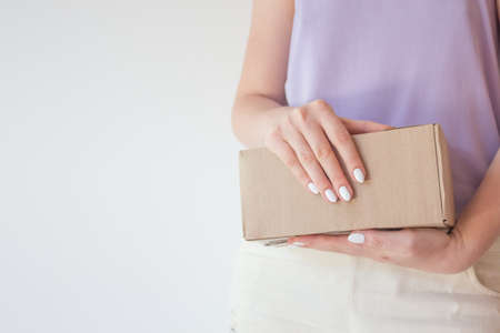 Beautiful girl with a parcel in hands, delivery concept. White manicure, box with orderの写真素材