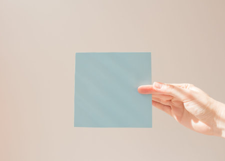 Blue square leaflet with hard shadows mock up on a white background in the hand of a young woman....