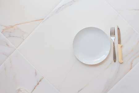Empty white plate with cutlery on a marble table, saucer, fork and knife. The concept of diet, fastingの写真素材