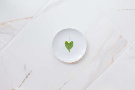 The concept of diet and weight loss, fasting and cleansing the body. Empty white plate on a white marble table. Detox the body with green foods.の写真素材