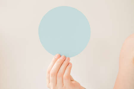 Round blue card with copy space in the hand of a young woman. Pastel blue color postcard layout. Informational round plate about a discount, opening, new product, advantageous offerの写真素材