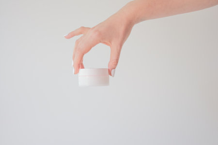 Plastic jar of cream in a female hand isolated on white. Professional cosmetics to restore skin youth, anti-aging cream. Skin care concept. Jar mockupの写真素材