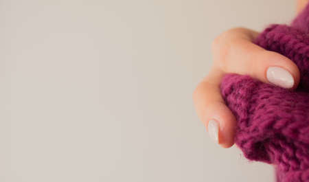 Knitted raspberry purple scarf in the hand of a young slender woman with a beautiful maicure. Knitted product close up mock up with copy space. Warm winter accessory.の写真素材