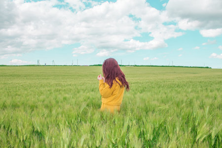 Beautiful girl with bright red hair is happy in a wheat field. Blue sky with small cloudless clouds,...