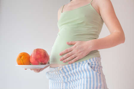 Pregnant woman is holding a bowl of fruit. Pregnant healthy food concept. Vitamins in fruits for pregnant women, a balanced diet, only fresh and healthy food.の写真素材