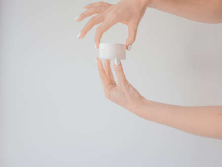 Plastic jar of cream in a female hand isolated on white. Professional cosmetics to restore skin youth, anti-aging cream. Skin care concept. Jar mockupの写真素材