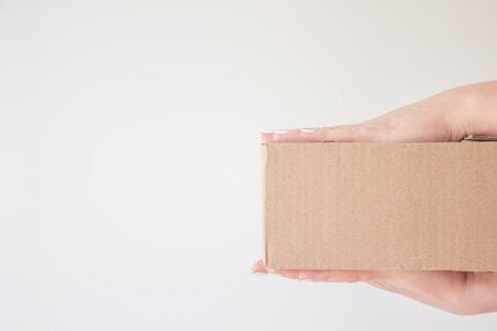 Cardboard box with a parcel in female hands. Concept of safe home delivery in a pandemic. Copy space. An order came from an online store.の写真素材
