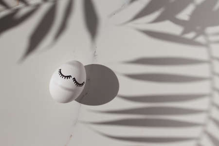 Easter holiday card with shadows from tropical palm leaves on white marble backgroundの写真素材