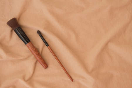 Makeup brushes and brushes still life on the background of beige fabric texture in folds of crumpled cotton in the afternoon. Cosmetic set with copy space for your design, website, ads.の写真素材