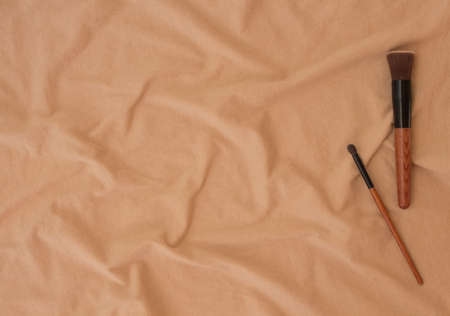 Makeup brushes and brushes still life on the background of beige fabric texture in folds of crumpled cotton in the afternoon. Cosmetic set with copy space for your design, website, ads.の写真素材