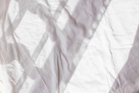 Crumpled white sheet with shadow and light from the window in the morning. The wrinkled background of a straightened bed after the night. White backgroundの写真素材