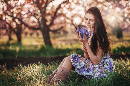 Portrait of a young beautiful girl with a bouquet of lavender in her hands in the spring gardenの写真素材