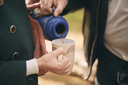Couple in love pours tea from a thermos into the cup to warm up on the streetの写真素材